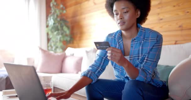 Stock video Happy african american woman using laptop and credit card in living room, in slow motion. Relaxation, communication, lifestyle and domestic life, unaltered.