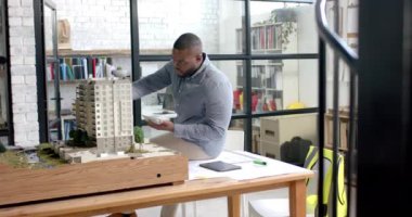 Afrika kökenli Amerikalı erkek mimar ofiste mimari model inşa ediyor, ağır çekimde. Yaratıcı iş, mimarlık, tasarım, gündelik ofis ve çalışma, değiştirilmemiş.