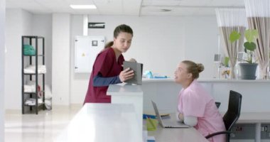 Kafkas kadın doktor hastanede resepsiyonistle konuşuyor, ağır çekimde. Hastane, takım çalışması, iletişim, tıp, sağlık ve iş, değiştirilmemiş.