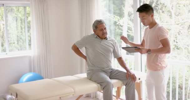 Různorodý Mužský Fyzioterapeut Tabletovým Vyšetřením Staršího Mužského Pacienta Zpomaleném Filmu — Stock video