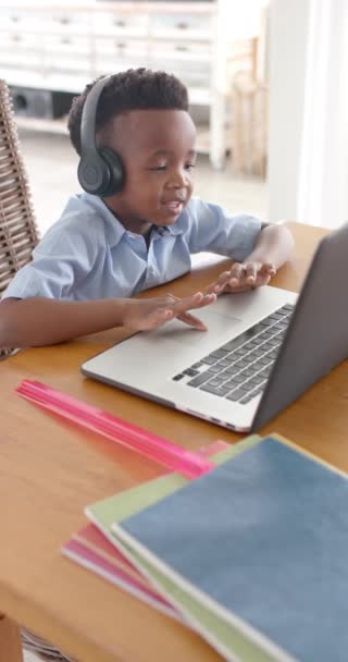 ヘッドフォンでアフリカ系アメリカ人の少年の垂直ビデオ オンラインクラスでラップトップを使用して スローモーション 子供時代 コミュニケーション 教育と国内生活 変更なし — ストック動画