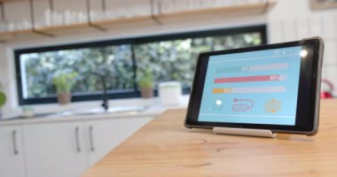 Akıllı ev arayüzü olan tablet mutfaktaki ahşap masada, ağır çekimde. İletişim, teknoloji ve ev hayatı.