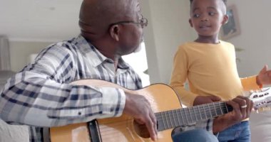 Mutlu Afro-Amerikan büyükbabası ve torunu gitar çalıyor, evde beşlik çakıyor, ağır çekimde. Aile, yaşam tarzı, çocukluk, müzik, birliktelik, rahatlama ve ev hayatı, değişmemiş.