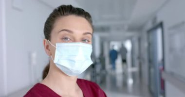 Koridorda yüz maskesi takan mutlu beyaz kadın doktor portresi, ağır çekimde. Hastane, ilaç, sağlık ve iş, değiştirilmemiş.