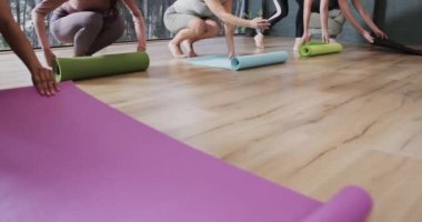 Yoga sınıfında kadın antrenörle birlikte yere paspas seren farklı kadınlara odaklanmış, ağır çekimde. Refah, zindelik, egzersiz ve sağlıklı yaşam tarzı, değişmemiş..