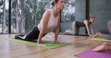 Yoga dersinde kadın koçla birlikte çocuk pozisyonunda poz veren farklı kadınlar, ağır çekimde. Refah, zindelik, egzersiz ve sağlıklı yaşam tarzı, değişmemiş..