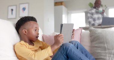 Afrika kökenli Amerikalı torun, dedesiyle tablet kullanıyor. Evde dizüstü bilgisayar kullanıyor. Ağır çekimde. Aile, yaşam tarzı, çocukluk, iletişim, rahatlama ve aile hayatı, değişmemiş..