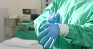 Midsection of caucasian female surgeon wearing medical gloves in operating theatre, slow motion. Hospital, surgery, medicine, healthcare and work, unaltered.