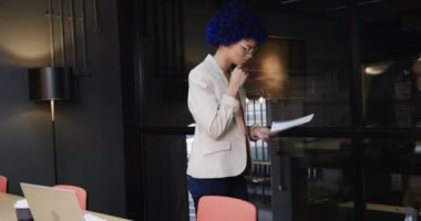 Mavi afro saçlı çift ırklı iş kadını toplantı odasında evrak okuyor, ağır çekimde. Günlük ofis, iş ve iş, değiştirilmemiş.