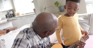 Mutlu Afro-Amerikan büyükbabası ve torunu evde birlikte gitar çalıyor, ağır çekimde. Aile, yaşam tarzı, çocukluk, müzik, birliktelik, rahatlama ve ev hayatı, değişmemiş.