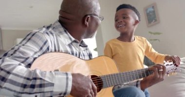 Mutlu Afro-Amerikan büyükbabası ve torunu evde birlikte gitar çalıyor, ağır çekimde. Aile, yaşam tarzı, çocukluk, müzik, birliktelik, rahatlama ve ev hayatı, değişmemiş.