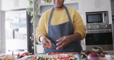 Önlüklü Afrikalı Amerikalı bir kadının orta bölümü mutfakta yemek hazırlıyor, ağır çekimde. Yemek, yemek, sebze, sağlıklı yaşam, refah ve ev hayatı, değişmemiş.