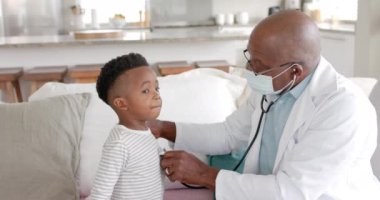 Kıdemli Afro-Amerikan erkek doktor, erkek hasta üzerinde steteskop kullanıyor, ağır çekimde. Ev ziyareti, kontrol, hijyen, sağlık hizmetleri, sağlık ve çocukluk, değiştirilmemiş.