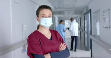 Koridorda yüz maskesi takan mutlu beyaz kadın doktor portresi, ağır çekimde. Hastane, ilaç, sağlık ve iş, değiştirilmemiş.