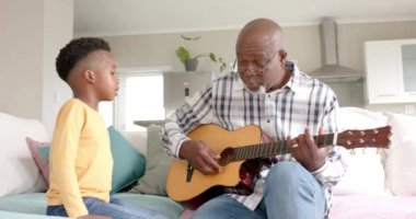 Mutlu Afro-Amerikan büyükbabası ve torunu evde gitar çalıp şarkı söylüyor, ağır çekimde. Aile, yaşam tarzı, çocukluk, müzik, birliktelik, rahatlama ve ev hayatı, değişmemiş.