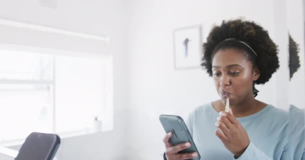 Wanita Afrika Amerika Menggosok Gigi Dan Menggunakan Smartphone Cermin Kamar — Stok Video