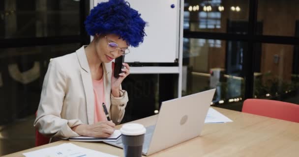 青いアフロがスマートフォンで話しているとデスクでノートパソコンを使用して出産ビジネス女性 スローモーション カジュアルオフィス ビジネス コミュニケーションと仕事 — ストック動画