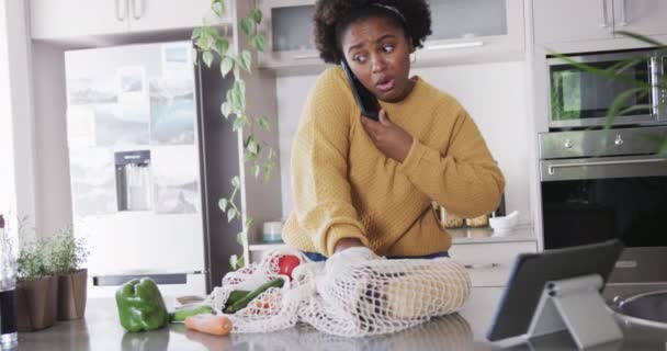 Lykkelig Afroamerikansk Kvinne Som Snakker Smarttelefon Pakker Matvarer Kjøkkenet Sakte – stockvideo