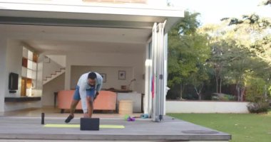 Odaklanmış Afro-Amerikan erkek fitness eğitimi güneşli bahçede güvertede geriliyor, ağır çekimde. Refah, zindelik ve sağlıklı yaşam tarzı, değişmedi..