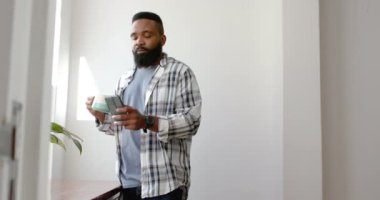 Afrika kökenli Amerikalı bir adam kahve içiyor ve evde akıllı telefon kullanıyor, ağır çekimde. Rahatlama, yaşam tarzı, iletişim ve ev hayatı, değişmemiş..