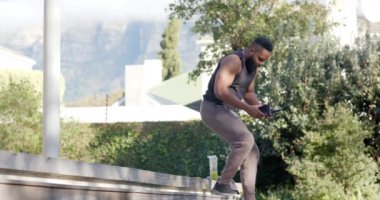 Afrika kökenli Amerikalı adam güneşli bahçede akıllı telefon ve kulaklıkla dinleniyor, ağır çekimde. Refah, zindelik, iletişim ve sağlıklı yaşam tarzı, değişmedi..