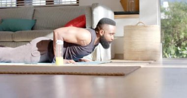 Odaklanmış Afro-Amerikan adam, güneşli evinde yoga yapıyor, ağır çekimde. Refah, zindelik ve sağlıklı yaşam tarzı, değişmedi..