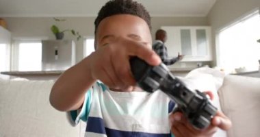 Afrikalı Amerikalı çocuk kanepede oturup video oyunları oynuyor, ağır çekimde. Yaşam tarzı, çocukluk, boş zaman ve ev hayatı, değişmemiş..