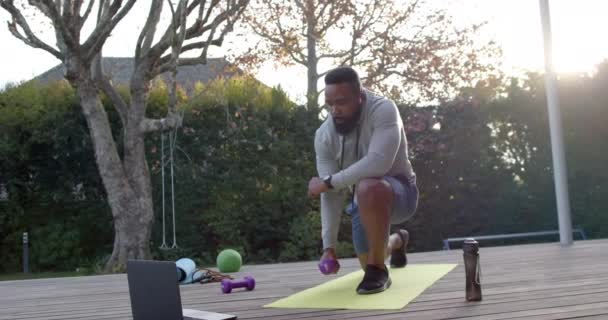 アフリカ系アメリカ人の男性のフィットネストレーニング日当たりの良い庭でデッキの重みで運動 スローモーション フィットネス 健康的なライフスタイル 変わらない — ストック動画