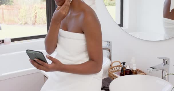 Mujer Birracial Feliz Con Toalla Cabeza Lavándose Cara Usando Teléfono — Vídeo de stock