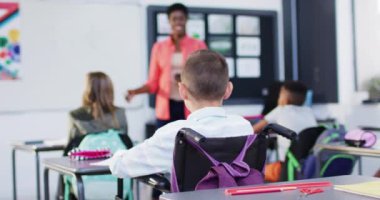 Kafkasyalı okul çocuğu çeşitli okul çocukları ve öğretmenlerle tekerlekli sandalyede oturuyor, ağır çekimde. İlköğretim, eğitim, öğrenme ve kapsayıcılık kavramı.