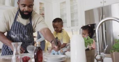 Oğlu ve kızı önlüklü mutlu Afro-Amerikan çifti mutfakta yemek hazırlıyor, ağır çekimde. Yemek, yemek, aile, birliktelik, yaşam tarzı ve aile hayatı, değişmedi..