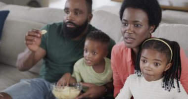Heyecanlı Afro-Amerikan ebeveynler, kızları ve oğulları TV 'de spor izliyorlar, ağır çekimde. Spor, eğlence, aile, birliktelik, yaşam tarzı ve ev hayatı, değişmemiş..
