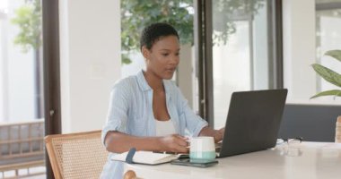 Afrika kökenli Amerikalı kadın masada oturuyor ve dizüstü bilgisayar kullanıyor, ağır çekimde. Yaşam tarzı, iletişim ve ev hayatı, evden çalışma, uzaktan çalışma, değişme yok..
