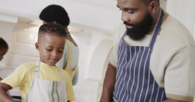 Oğlu ve kızı önlüklü mutlu Afro-Amerikan çifti mutfakta yemek hazırlıyor, ağır çekimde. Yemek, yemek, aile, birliktelik, yaşam tarzı ve aile hayatı, değişmedi..