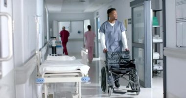 Afrika kökenli Amerikalı erkek doktor hastanenin koridorunda tekerlekli sandalyeyle yürüyor ve itiyor, ağır çekimde. Hastane, ilaç, sağlık ve iş, değiştirilmemiş.