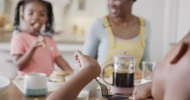 Oğlu ve kızı olan mutlu Afro-Amerikan annesi yemek odasında yemek yiyor, ağır çekimde. Yemek, yemek, aile, birliktelik, yaşam tarzı ve aile hayatı, değişmedi..