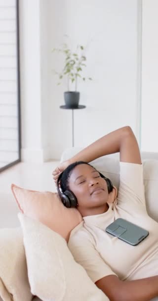 Vertical Video African American Woman Using Headphones Smartphone Sofa Slow — Stock Video