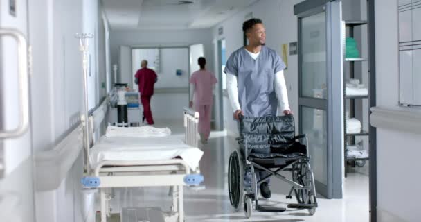Αφροαμερικάνος Γιατρός Περπατάει Και Σπρώχνει Αναπηρικό Καροτσάκι Στο Νοσοκομείο Αργή — Αρχείο Βίντεο