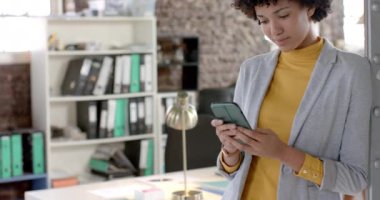 Focused biracial casual businesswoman using smartphone in office in slow motion. Business, technology and work, unaltered.