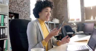 Happy biracial casual businesswoman using smartphone in office in slow motion. Business, technology and work, unaltered.