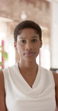 Vertical video of portrait of happy african american casual businesswoman in office in slow motion. Business and work, unaltered.