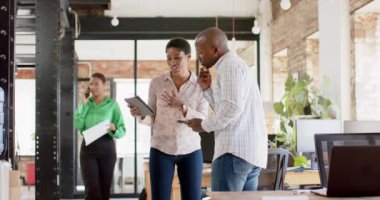 Mutlu Afro-Amerikan meslektaşları tablet kullanıyor ve ofiste işleri tartışıyor, ağır çekimde. İş, beyin fırtınası, teknoloji ve takım çalışması, değiştirilmemiş.