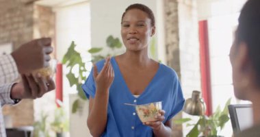 Mutlu Afrikalı Amerikalı meslektaşlar iş tartışıyor ve yaratıcı ofiste öğle yemeği yiyorlar, ağır çekimde. İş, beyin fırtınası, yemek ve takım çalışması, değiştirilmemiş.