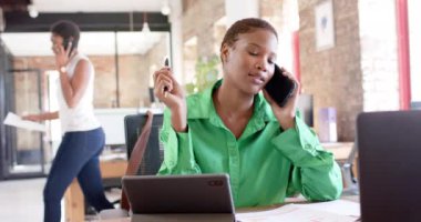 Happy african american casual businesswoman talking on smartphone in office in slow motion. Business, work and technology, unaltered.