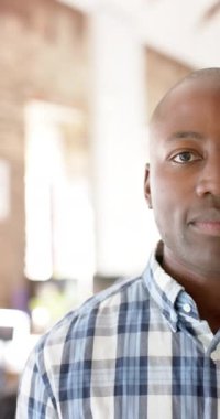 Vertical video of portrait of happy african american casual businessman in office in slow motion. Business and work, unaltered.