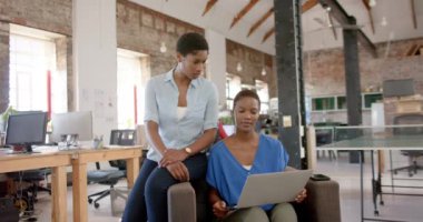 Laptop kullanan ve yaratıcı ofiste konuşan Afrikalı Amerikalı kadın meslektaşlar, yavaş çekim. İş, teknoloji ve takım çalışması, değiştirilmemiş.