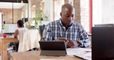 Focused african american casual businessman using tablet and taking notes in office in slow motion. Business, work and technology, unaltered.
