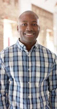 Vertical video of portrait of happy african american casual businessman in office in slow motion. Business and work, unaltered.