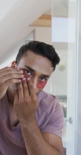 Vertical Video Latino Man Applying Eye Masks Looking Bathroom Mirror — Stock Video