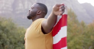 Portrait of african american man holding flag of usa in garden, slow motion. Patriotism, celebartion and lifestyle, unaltered.